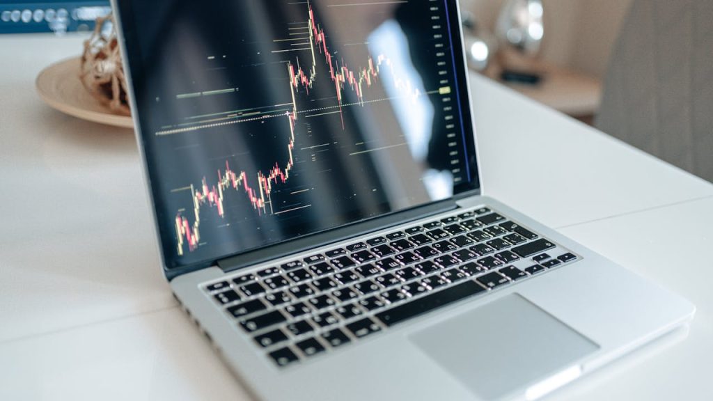 Laptop showing cryptocurrency market data on a white table, indoors.